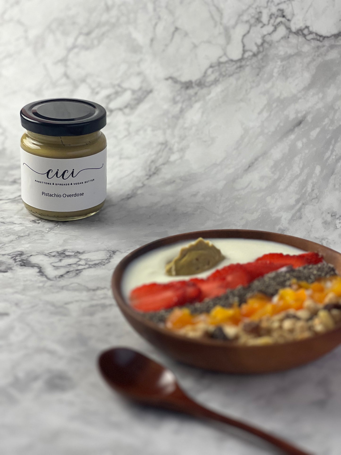 wooden bowl contains yoghurt and fresh fruits with pistachio cream spread at the back.